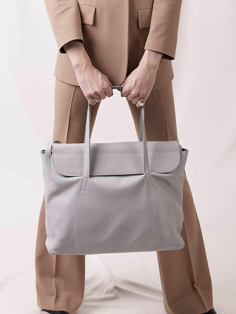 Person in beige suit holding large light grey leather tote bag with top handles
