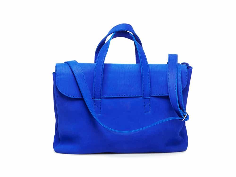 Vivid blue leather handbag with top handles and shoulder strap on white background