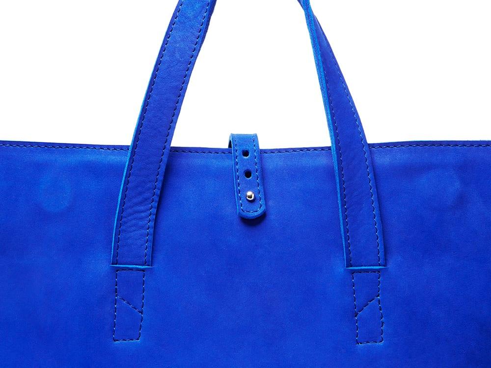 Close-up of a bright blue leather tote bag with double handles and metal stud detail