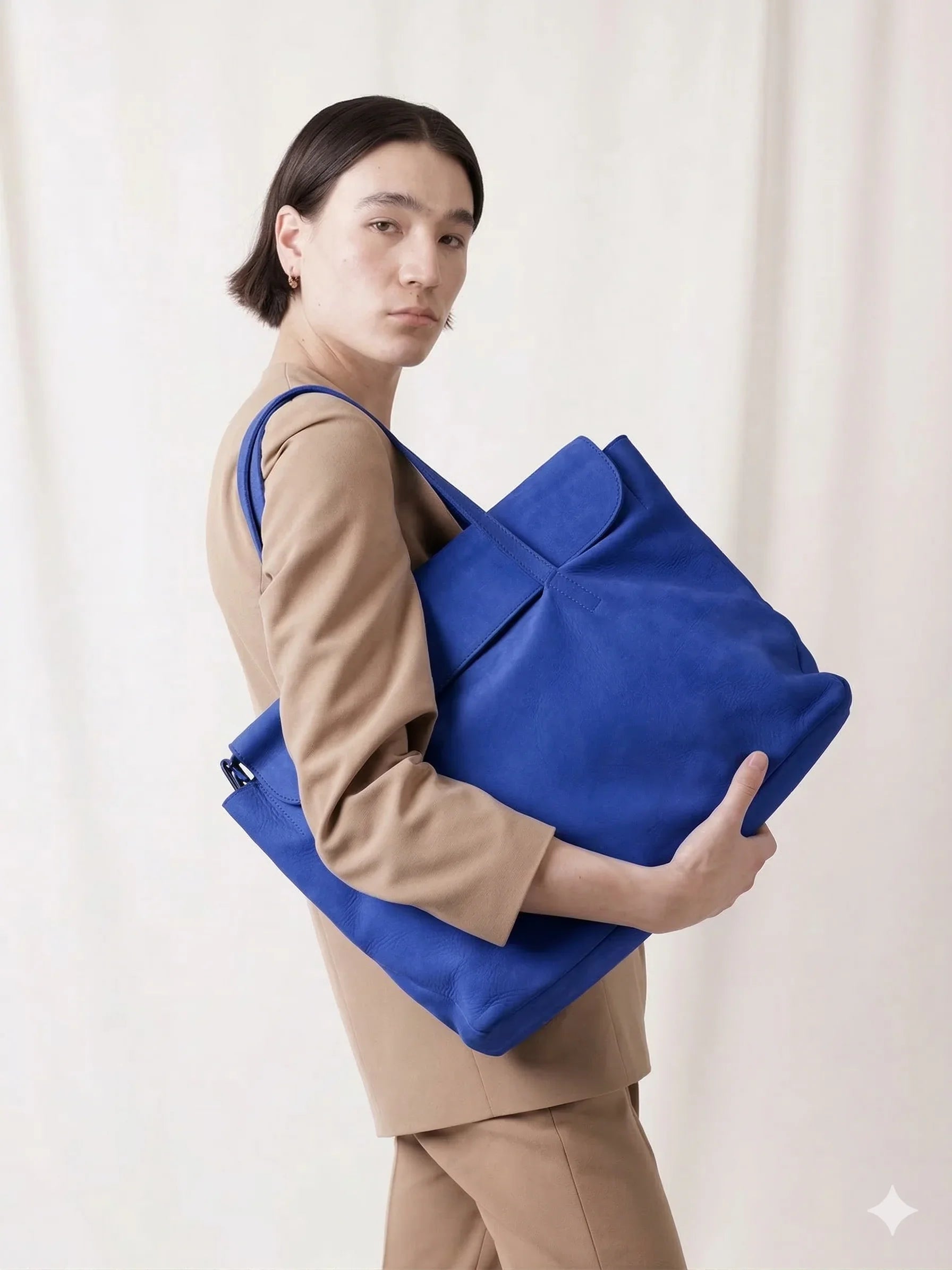 Person in beige suit holding large blue leather tote bag against light background