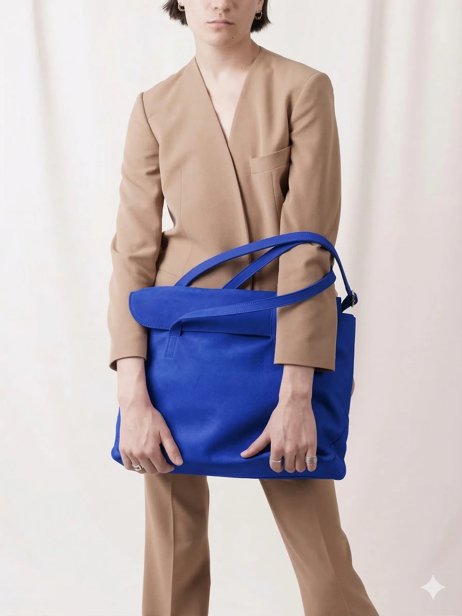 Person in tan suit holding large blue leather bag, modern minimalist fashion