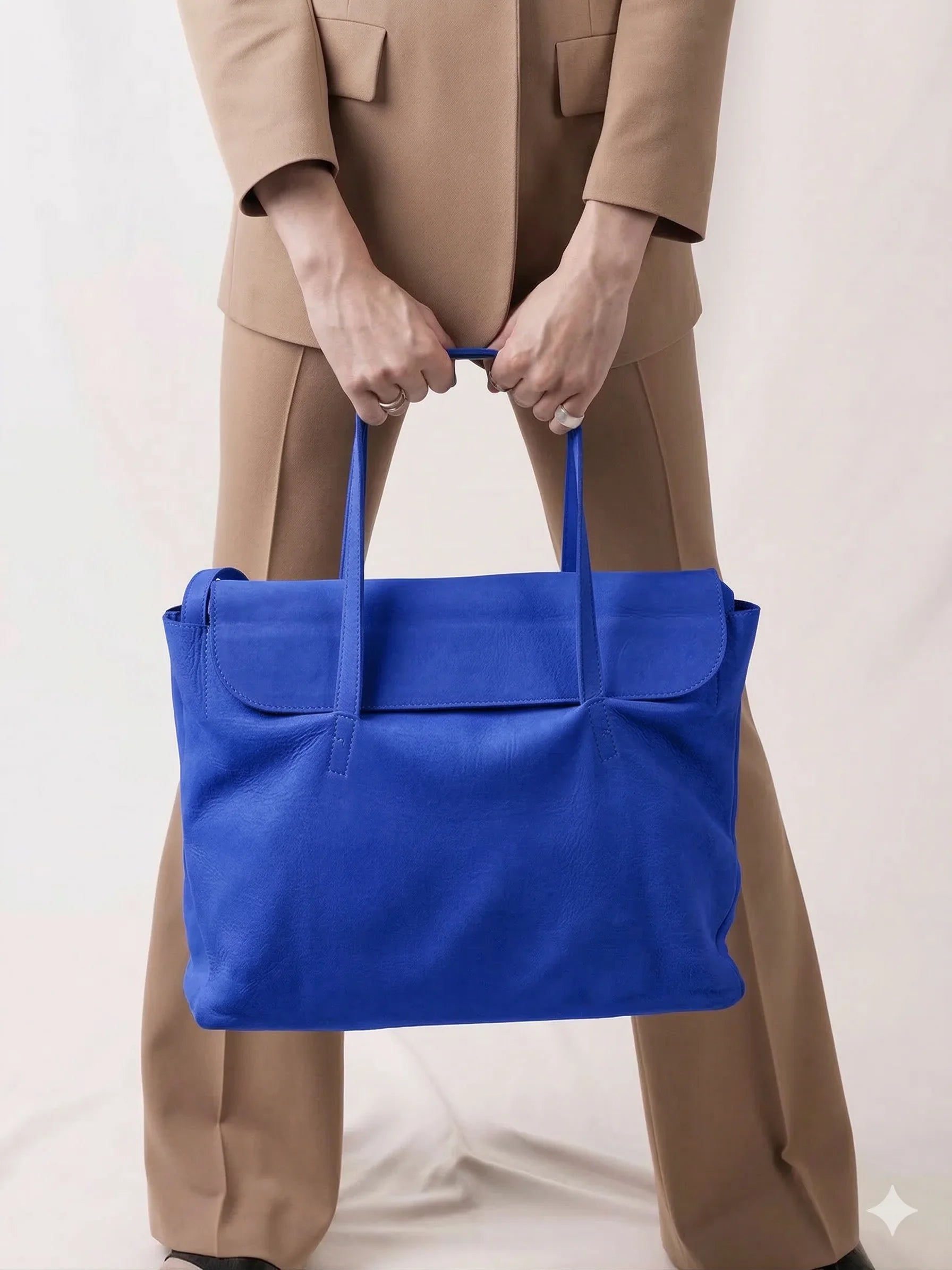 Person in tan suit holding large blue leather tote bag