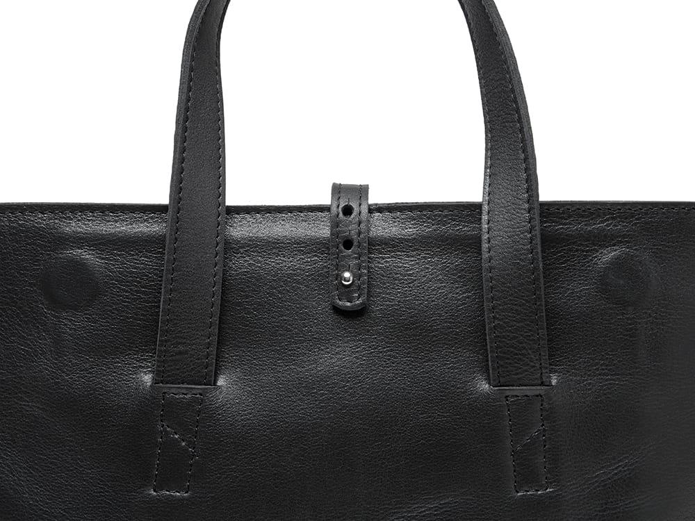 Close-up of black leather tote bag with sturdy handles and buttoned strap detail